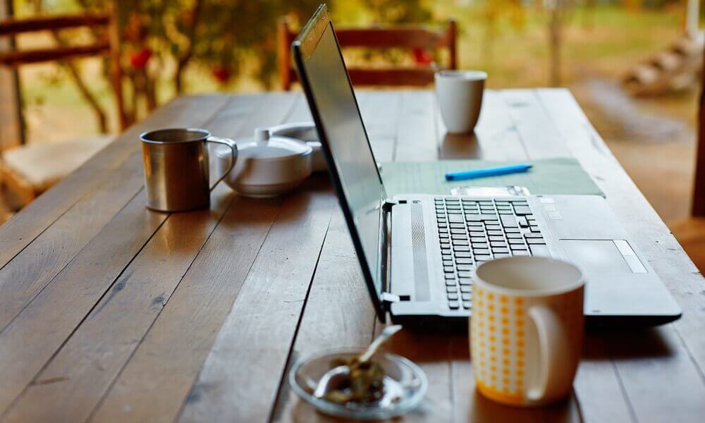 computer, coffee, and tea set up on a picnic table as a remote office environment