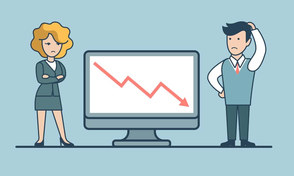 business man and business woman standing by a computer with arrow trending downward.